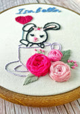 Load image into Gallery viewer, Embroidery hoop with a bunny in a teacup surrounded by flowers and yarn, on a light background.