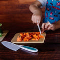 Load image into Gallery viewer, Child cutting carrots on a wooden board with a knife, wearing a blue apron with British flags.