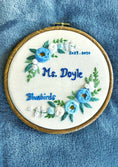 Load image into Gallery viewer, Embroidery hoop with floral design and text on a blue fabric background