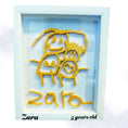 Load image into Gallery viewer, Framed artwork with yellow cut-out figures and 'Zara' written below, on a light blue background.