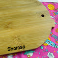 Load image into Gallery viewer, Wooden cutting board with 'Shamsa' branding on a colorful fabric background
