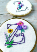 Load image into Gallery viewer, Two embroidery hoops with floral designs and embroidered names on a wooden surface.
