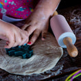 Load image into Gallery viewer, Children's hands using a cookie cutter on dough with a rolling pin nearby.
