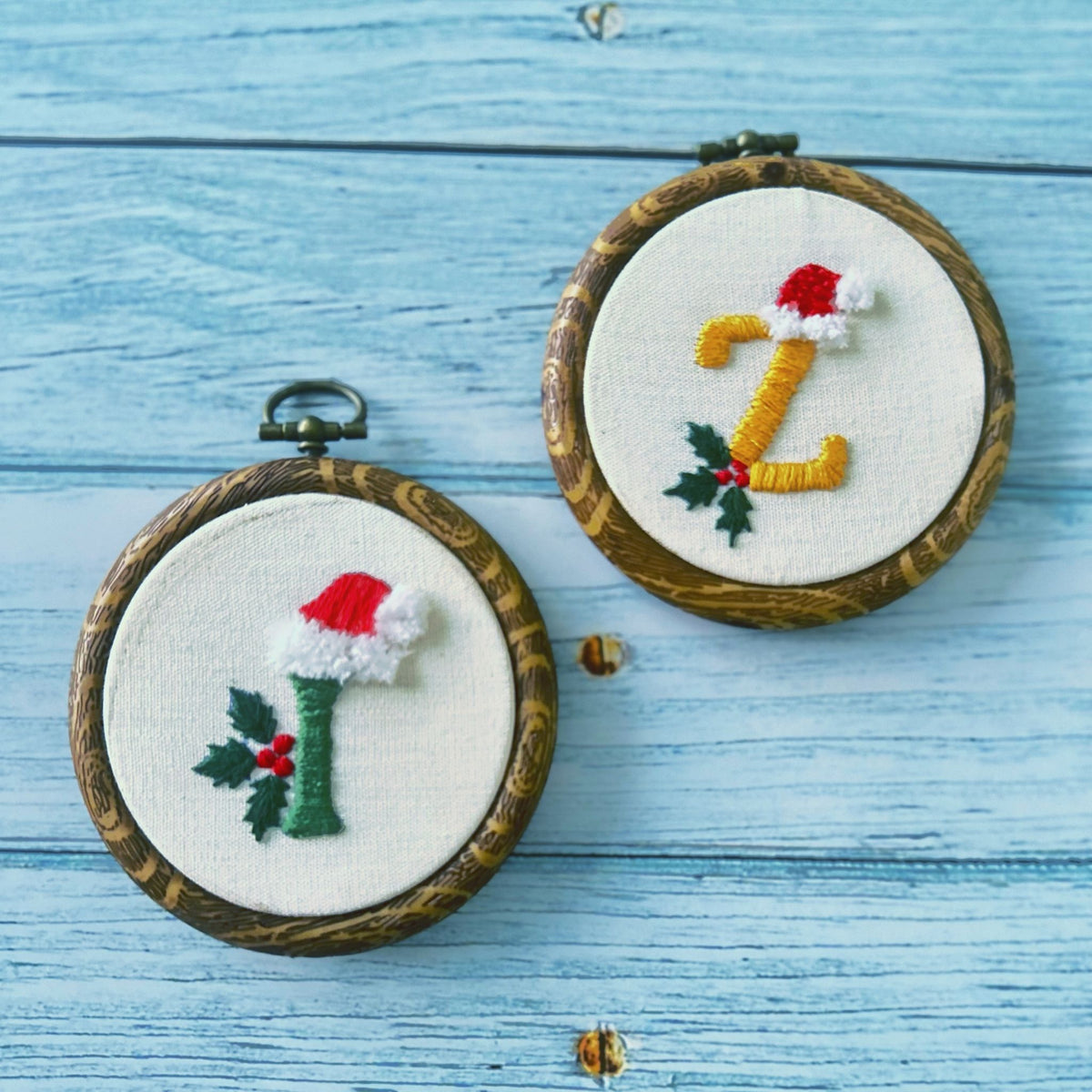 Two mini hand embroidered Christmas ornaments with initials I and Z wearing Santa hats with holly, made in Dubai