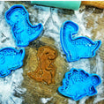 Load image into Gallery viewer, Dinosaur-shaped cookie cutters on a wooden surface with a cookie between them.
