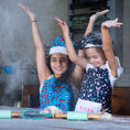 Load image into Gallery viewer, Two children in aprons with raised arms in a kitchen setting
