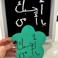 Load image into Gallery viewer, Hand holding a green flower-shaped card with Arabic text in front of a blackboard with similar text.
