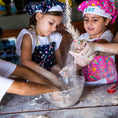 Load image into Gallery viewer, Two young girls in chef hats and aprons mixing flour in a bowl.
