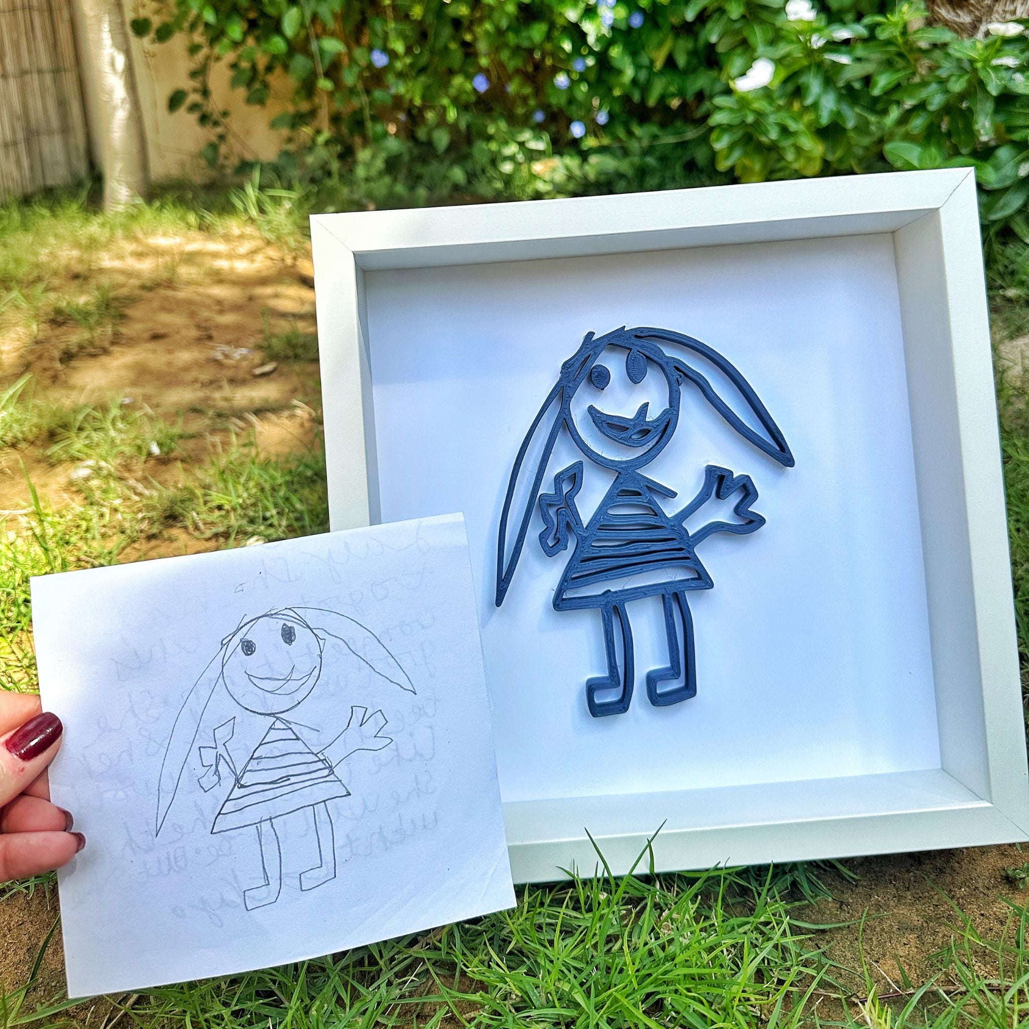 Framed paper cutout of a stick figure with a dress, next to a hand-drawn version outdoors.