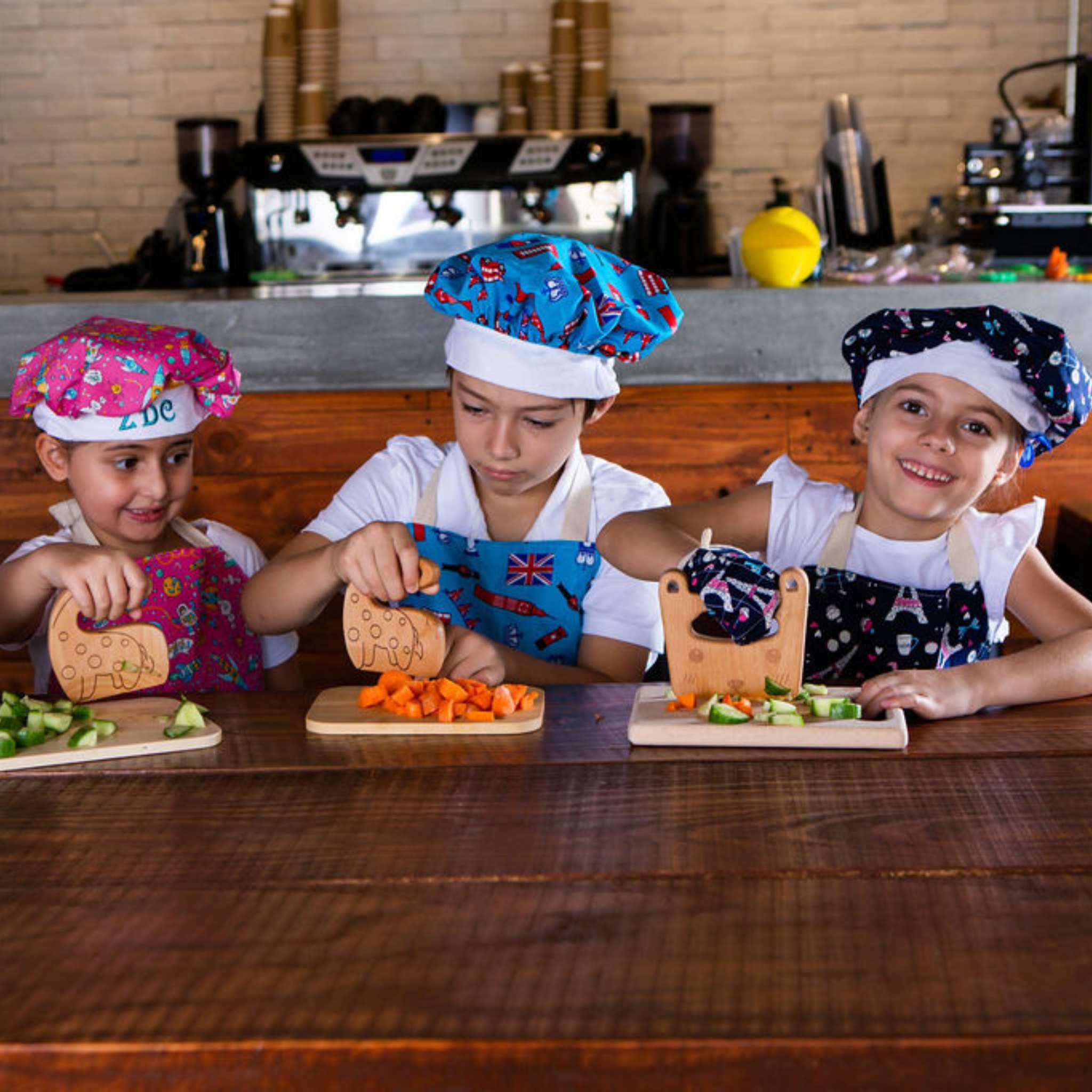 Three children in chef hats and aprons preparing food in a kitchen.
