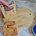 Load image into Gallery viewer, Wooden cutting board with animal shapes and 'Isabella' engraving on a stone surface.
