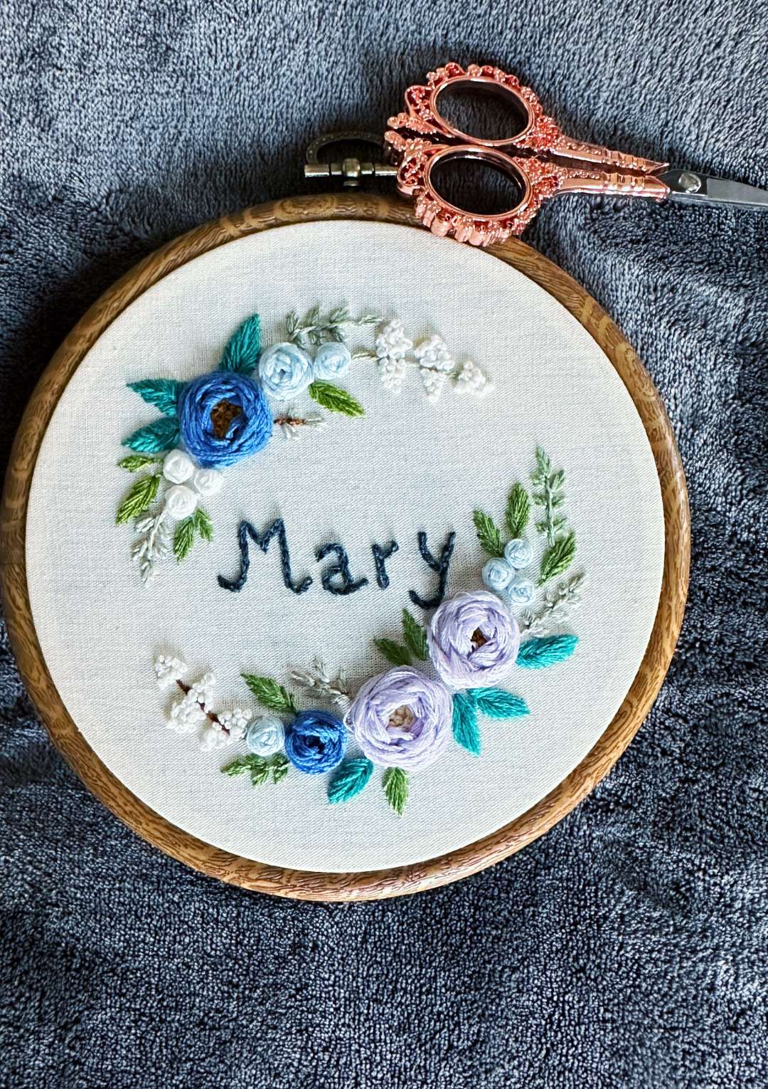 Embroidery hoop with floral design and 'Mary' text on a textured surface