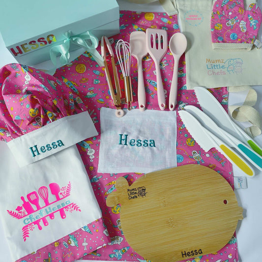 Kitchen set with pink apron, utensils, and cutting board on a colorful background with 'Hessa' branding.