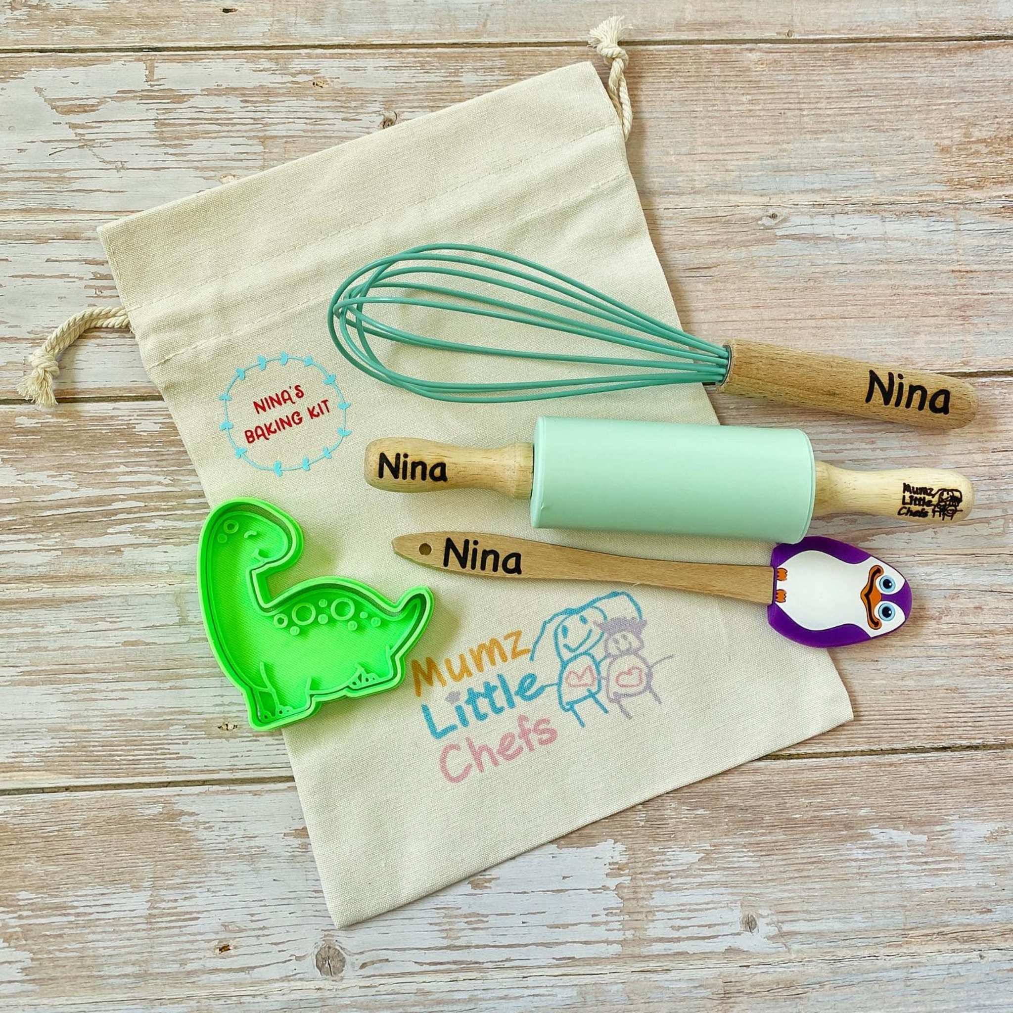 Children's baking tools including a whisk, rolling pin, and cookie cutter on a 'Mumz Little Chefs' branded bag.