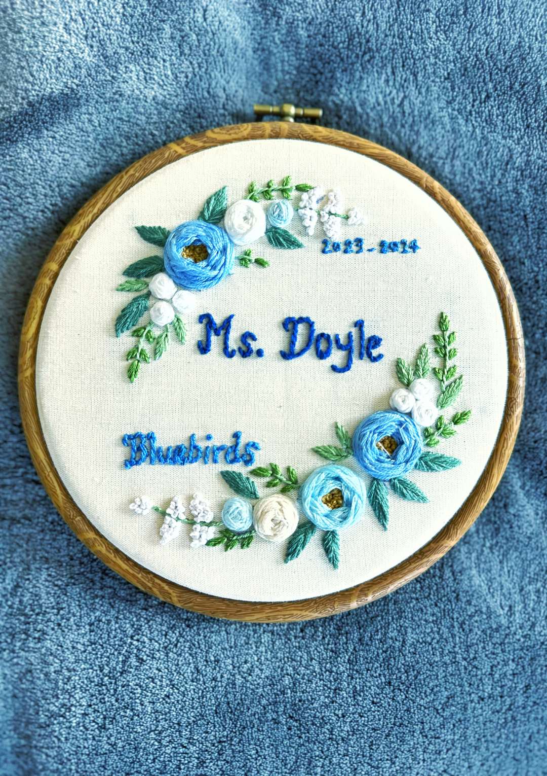Embroidery hoop with floral design and text on a blue fabric background