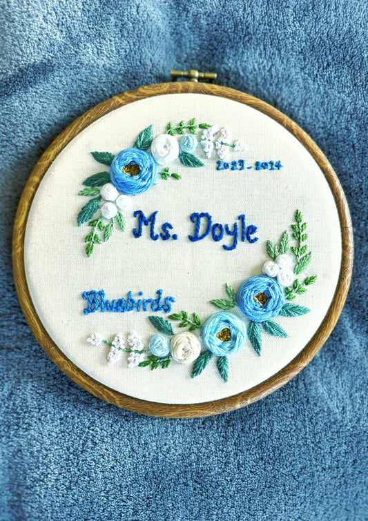 Embroidery hoop with floral design and text on a blue fabric background