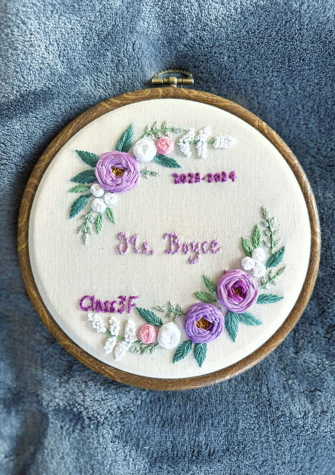 Embroidery hoop with floral design and text on a blue fabric background