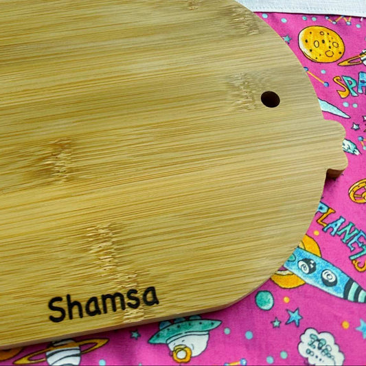 Wooden cutting board with 'Shamsa' branding on a colorful fabric background